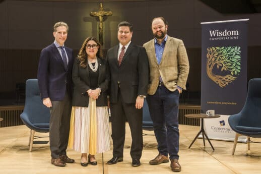 Noah Feldman, Mary Ann Gomez Orta, Gerson Moreno-Riaño and Ross Douthat standing on the stage in Christ Chapel at Cornerstone University near a banner that says Wisdom Conversations