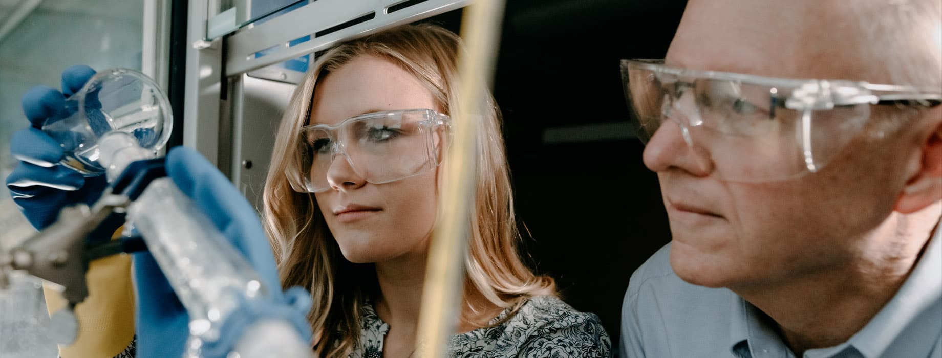 Female college student pouring a beaker while a male professor looks on