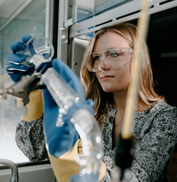 Female college student pouring a beaker while a male professor looks on