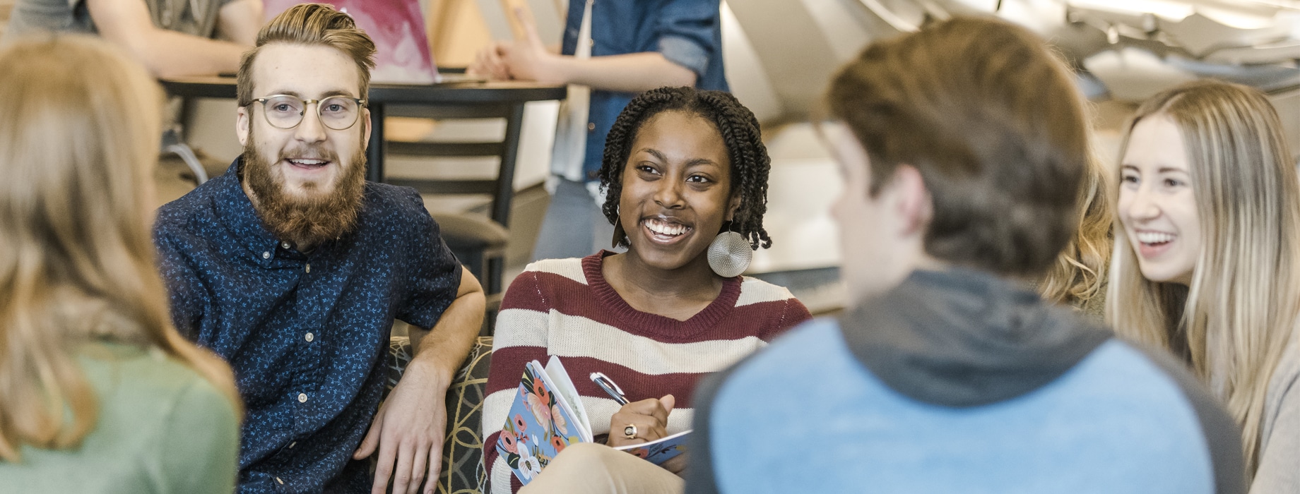 Male and female college students sitting in the lobby of Christ Chapel at Cornerstone University while a female student takes writes notes in a notebook