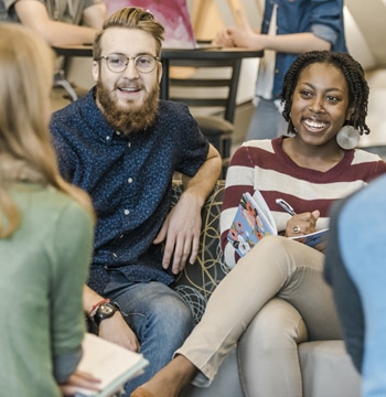 Male and female college students sitting in the lobby of Christ Chapel at Cornerstone University while a female student takes writes notes in a notebook