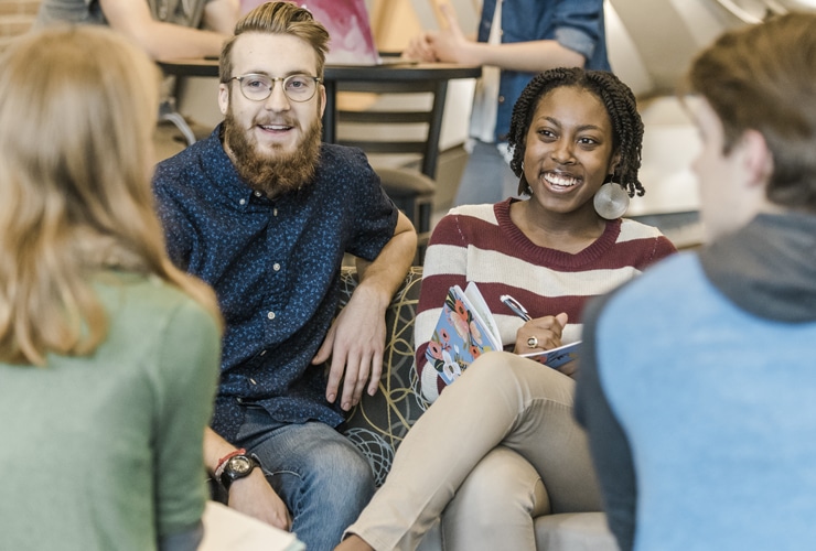 Male and female college students sitting in the lobby of Christ Chapel at Cornerstone University while a female student takes writes notes in a notebook