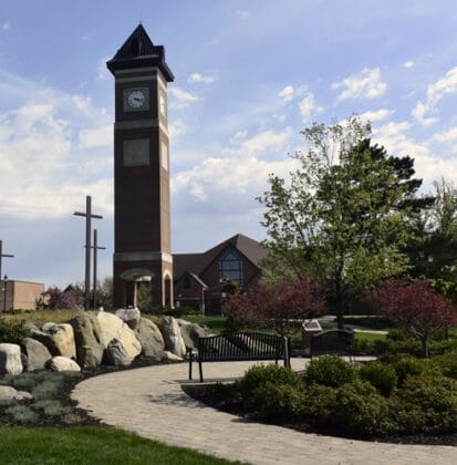 Tall clock tower, with a building and three crosses in the background in the Cornerstone University campus