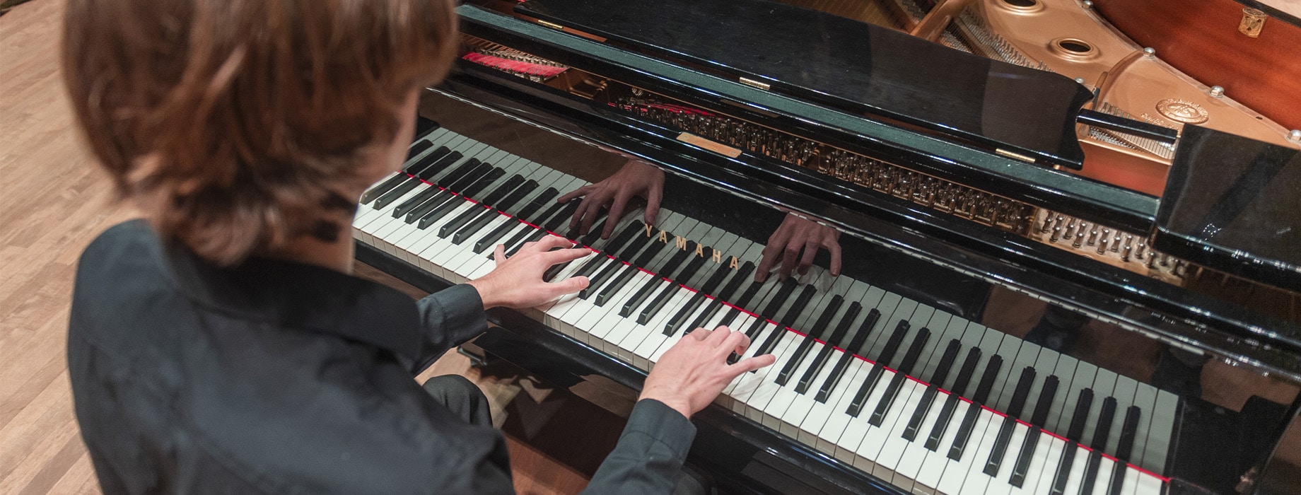 Male playing a grand piano in Matthews Performing Arts Center at Cornerstone University