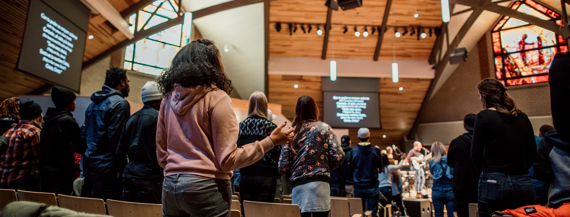 College students worshipping with raised hands and a band in the sanctuary of Christ Chapel at Cornerstone University