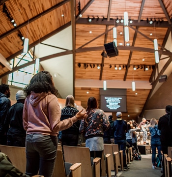 College students worshipping with raised hands and a band in the sanctuary of Christ Chapel at Cornerstone University