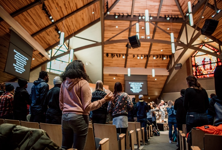 College students worshipping with raised hands and a band in the sanctuary of Christ Chapel at Cornerstone University
