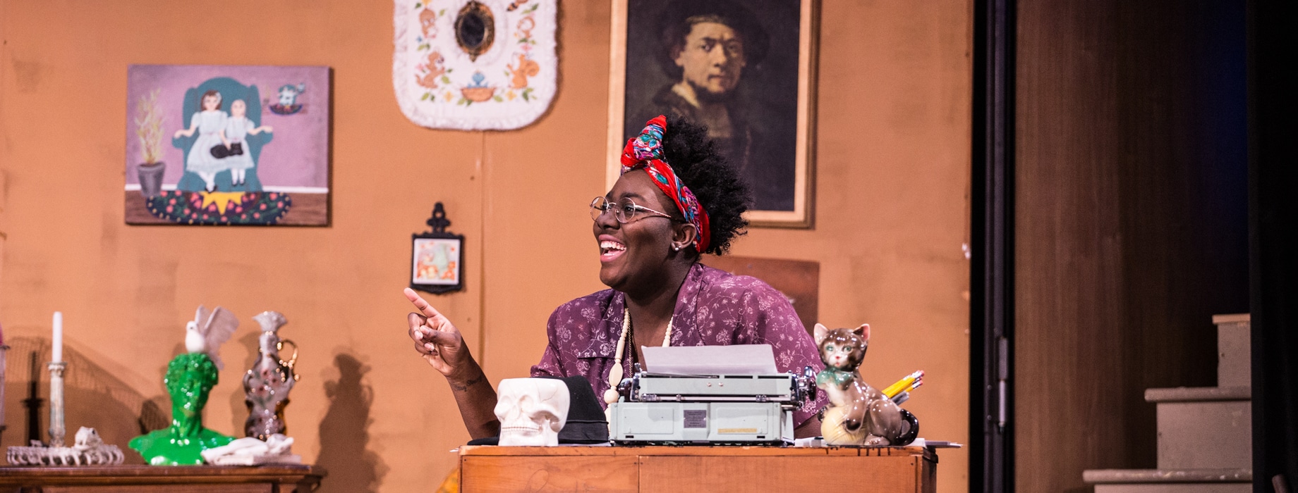 Female college student actor sitting at a desk with a typewriter for a theatre production at Cornerstone University