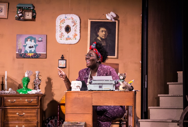 Female college student actor sitting at a desk with a typewriter for a theatre production at Cornerstone University
