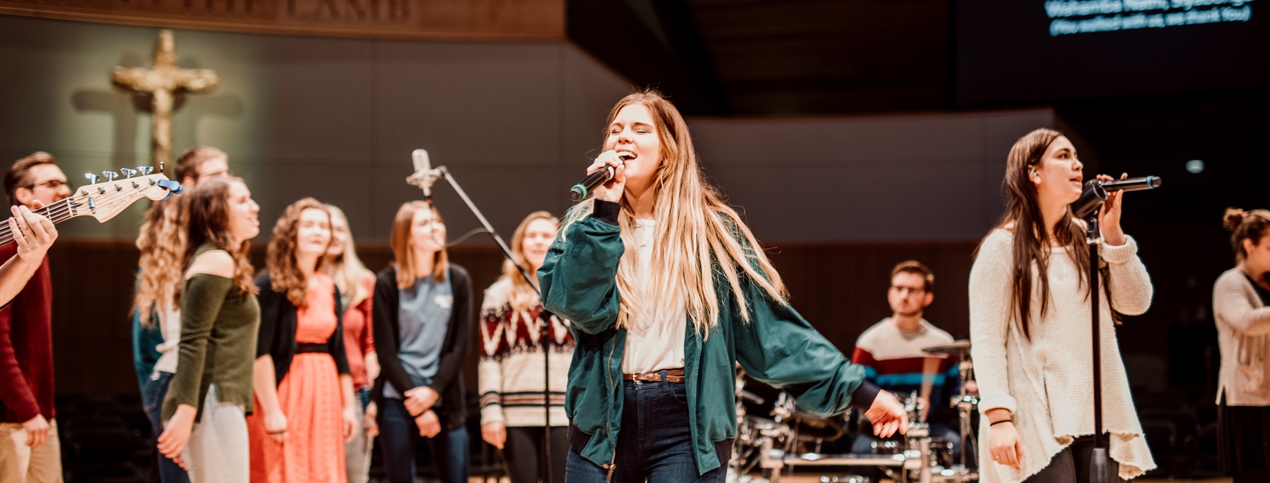 Female students leading singing with microphones on stage in Christ Chapel at Cornerstone University