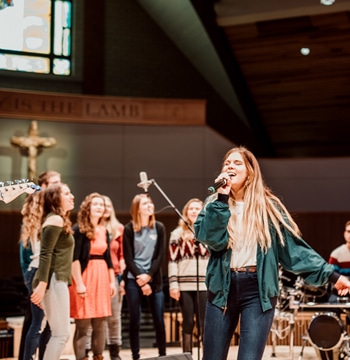 Female students leading singing with microphones on stage in Christ Chapel at Cornerstone University