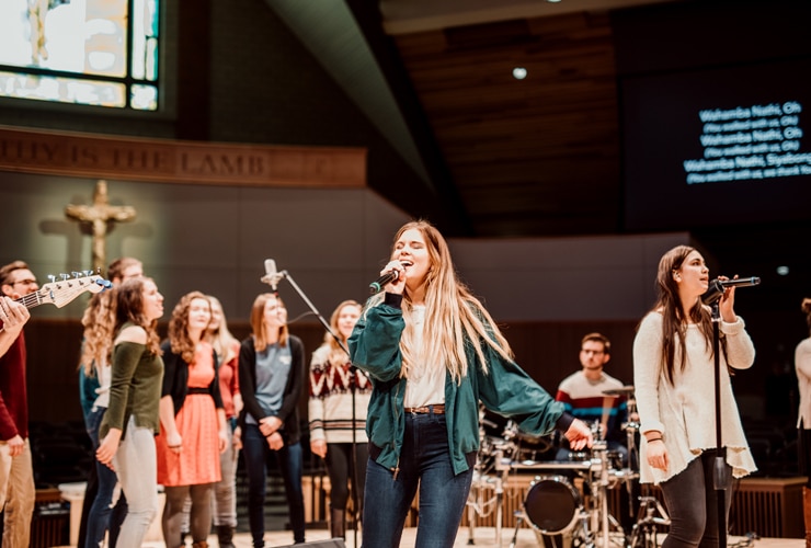 Female students leading singing with microphones on stage in Christ Chapel at Cornerstone University