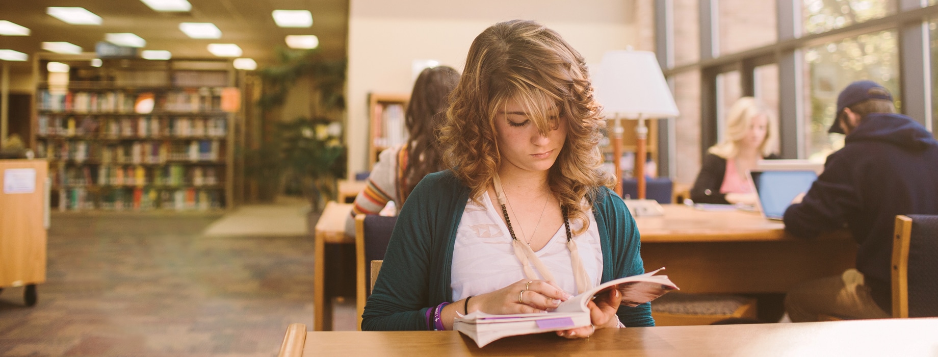 Female reading a book at a wooden table in Miller Library at Cornerstone University