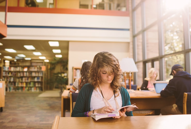 Female reading a book at a wooden table in Miller Library at Cornerstone University