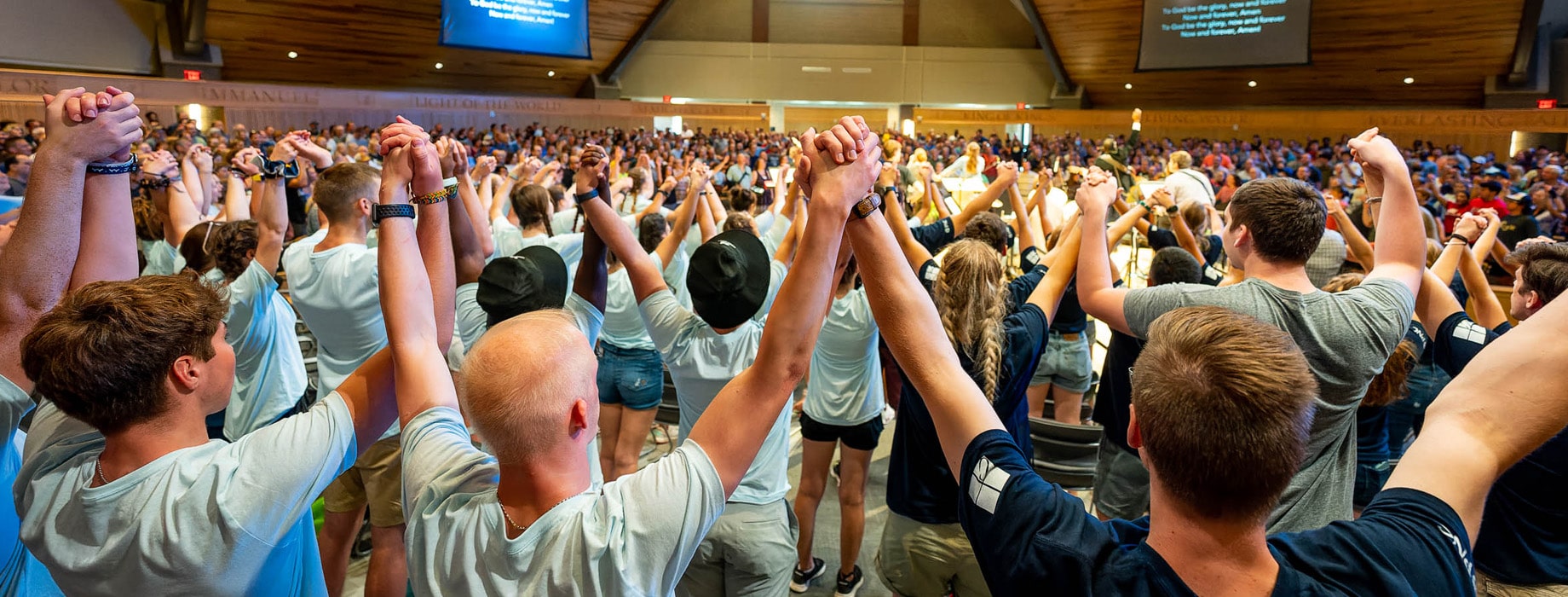 College students holding hands raised in the air while worshipping in the round in Christ Chapel at Cornerstone University