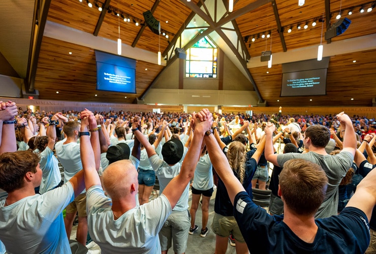 College students holding hands raised in the air while worshipping in the round in Christ Chapel at Cornerstone University