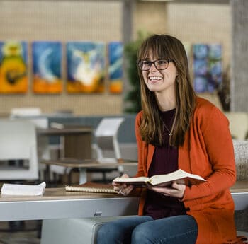Female seminary student holding a Bible while sitting in the lobby of Grand Rapids Theological Seminary