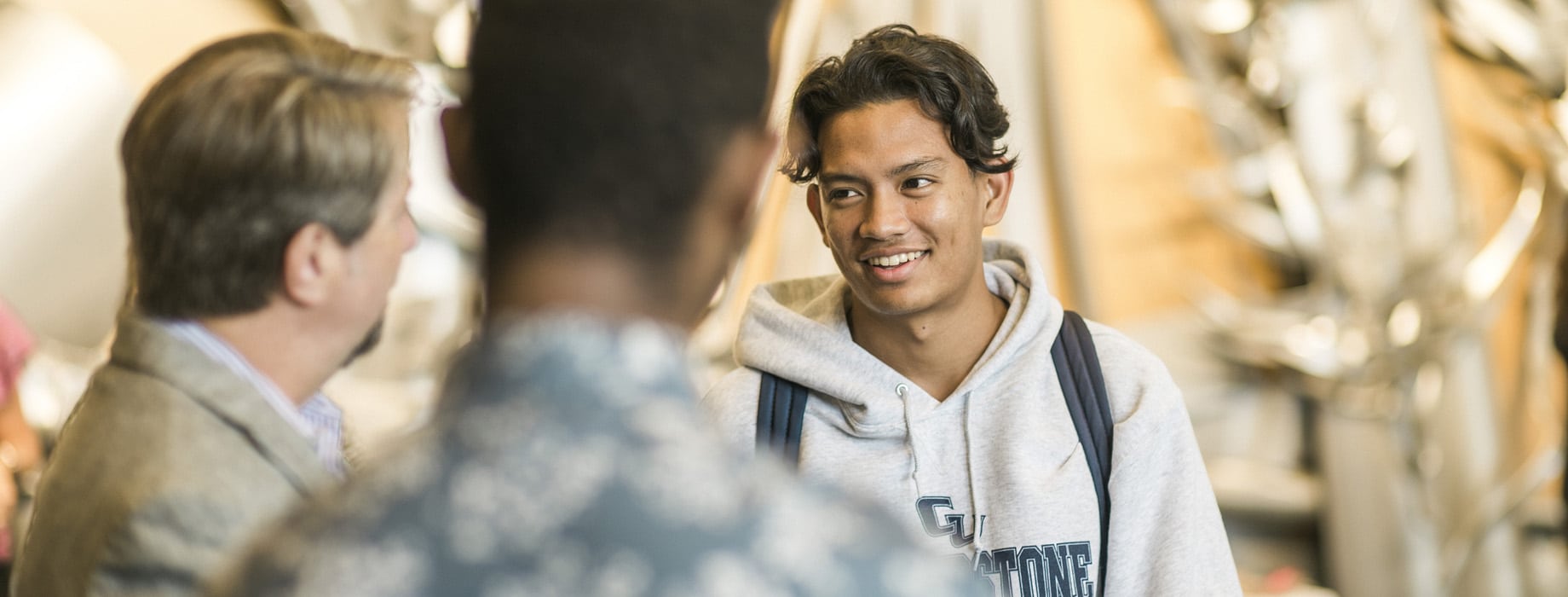 Male Cornerstone University students talking with a staff member in the lobby of Christ Chapel