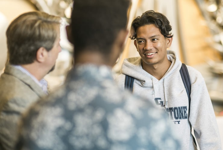 Male Cornerstone University students talking with a staff member in the lobby of Christ Chapel