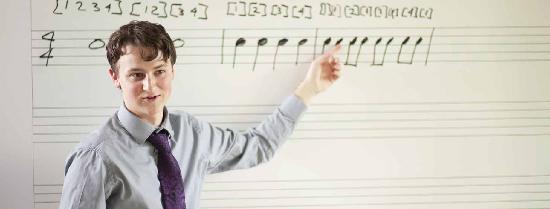 Male college student pointing to musical notation on a whiteboard in a classroom