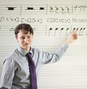Male college student pointing to musical notation on a whiteboard in a classroom