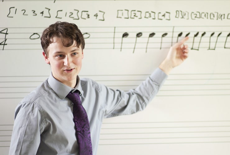 Male college student pointing to musical notation on a whiteboard in a classroom