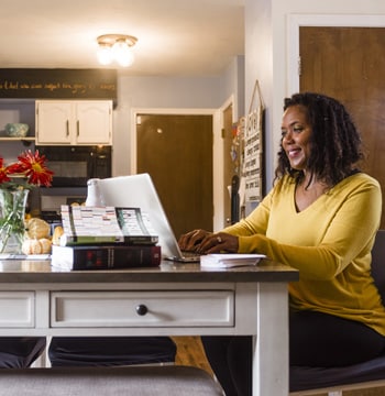 Adult female student typing on a laptop at a kitchen table