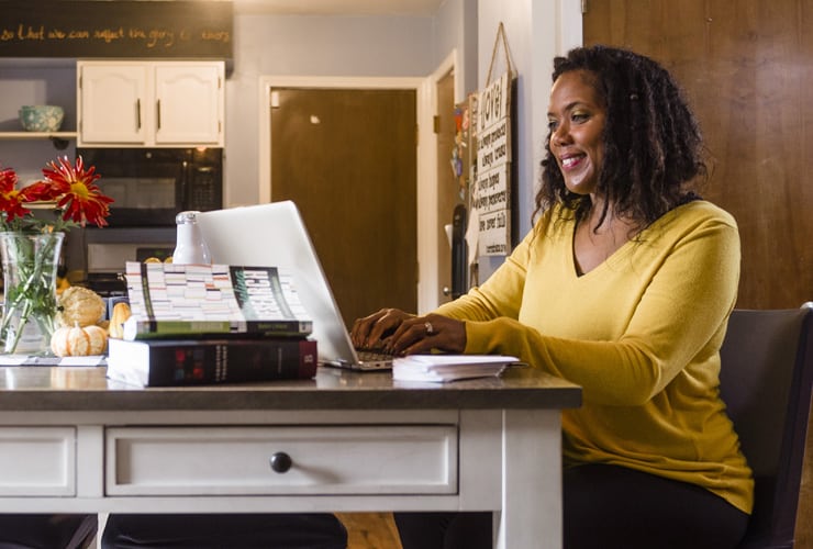 Adult female student typing on a laptop at a kitchen table