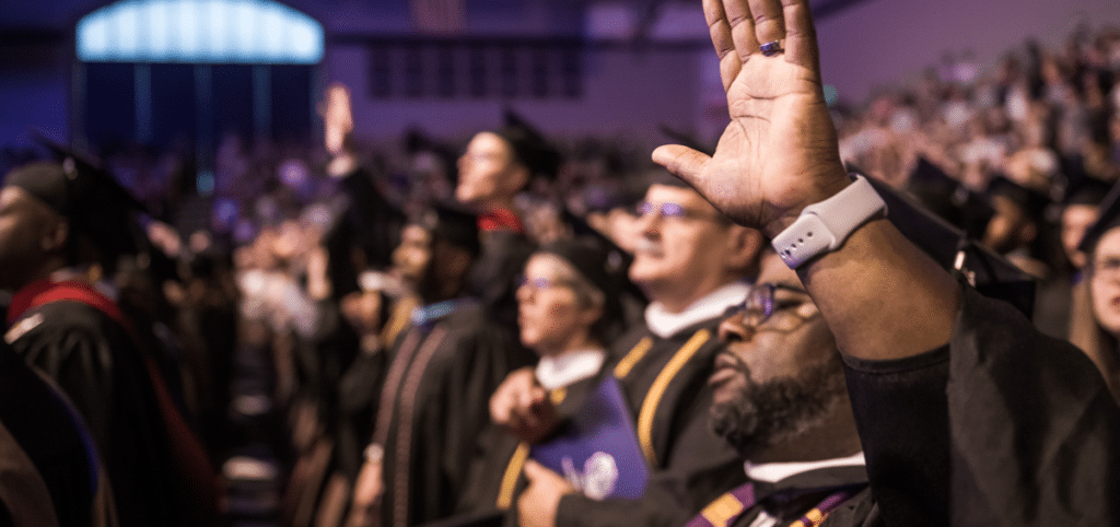 Adult male graduate student raises his hand in worship during Commencement at Cornerstone University