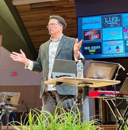 Ryan Bomberger speaks from stage in Christ Chapel sanctuary at Cornerstone University with presentation screen behind him