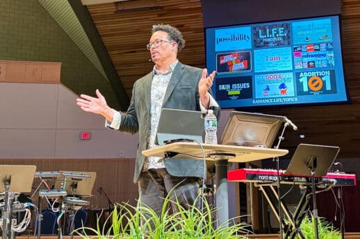 Ryan Bomberger speaks from stage in Christ Chapel sanctuary at Cornerstone University with presentation screen behind him