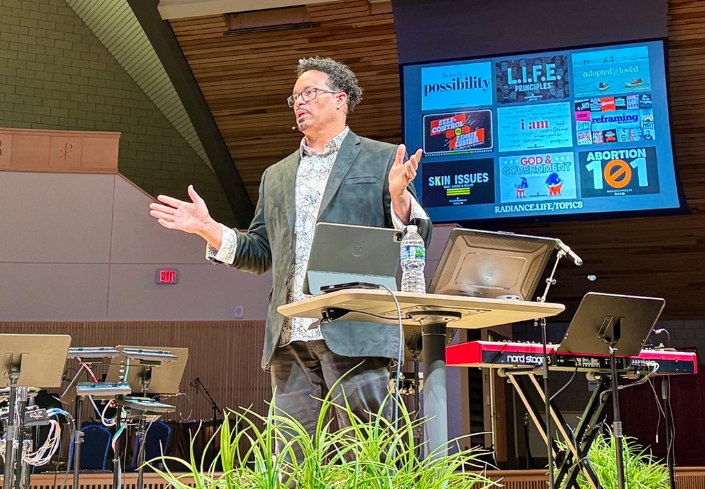 Ryan Bomberger speaks from stage in Christ Chapel sanctuary at Cornerstone University with presentation screen behind him