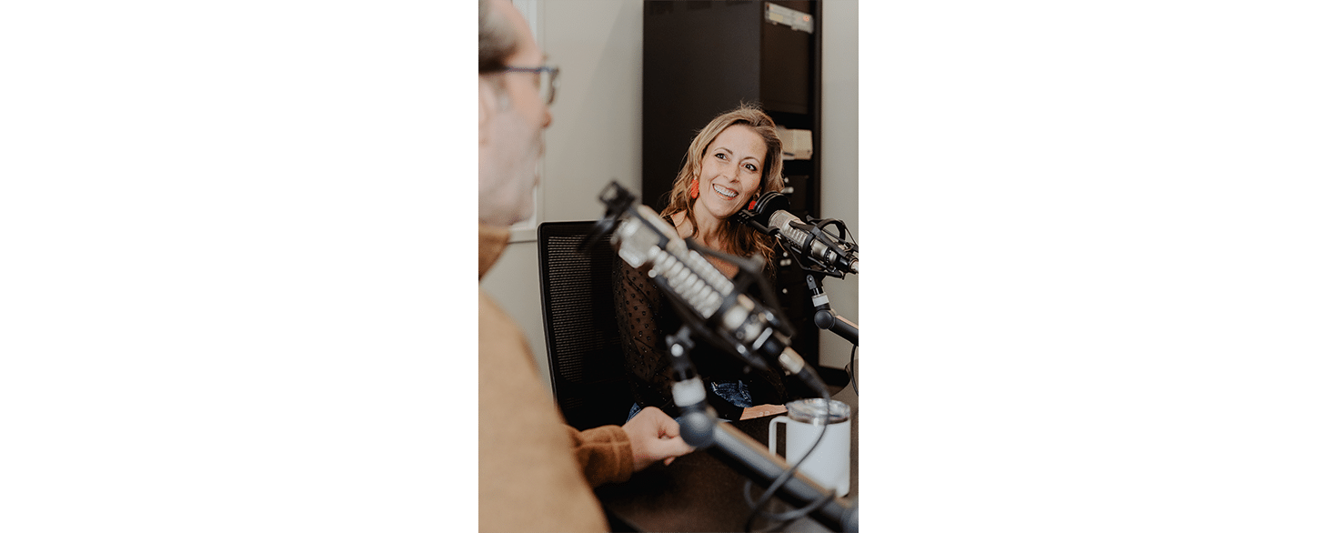 Female and male on-air announcers sitting at wooden desk with microphones