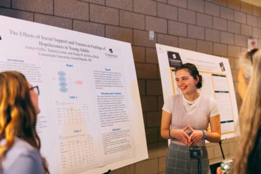 A female student presenting academic research on a poster to a crowd of individuals