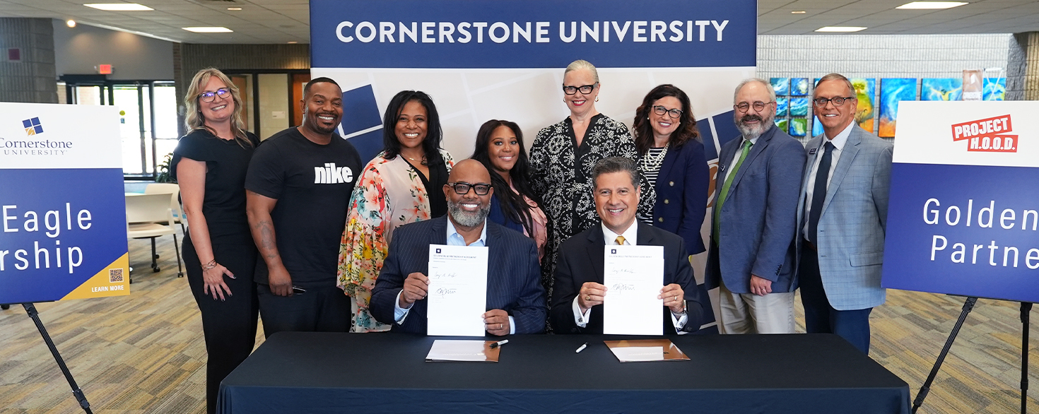 Pastor Corey Brooks and Dr. Gerson Moreno-Riaño display the signed Golden Eagle Partnership agreement while surrounded by members of the leadership team from Project H.O.O.D. and Cornerstone University