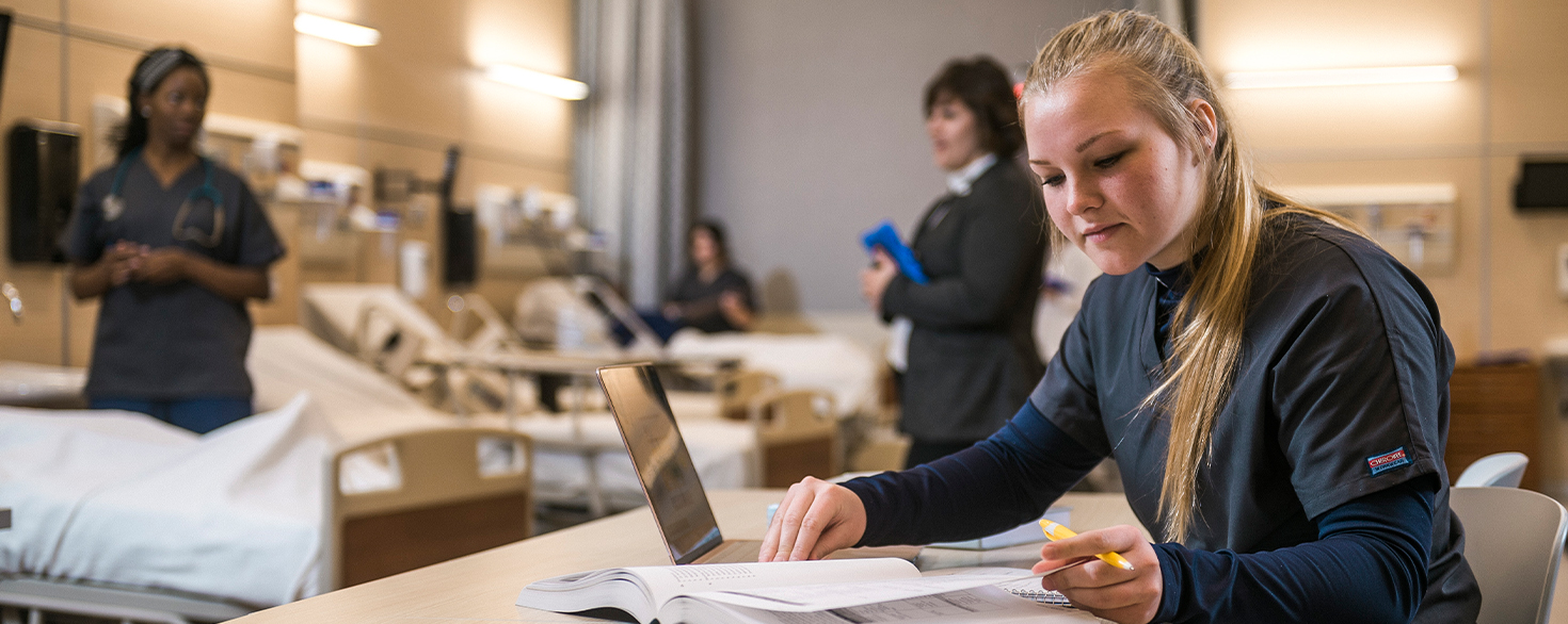 Cornerstone University female nursing student studies in simulation lab at the De Witt Center for Nursing while reading a textbook